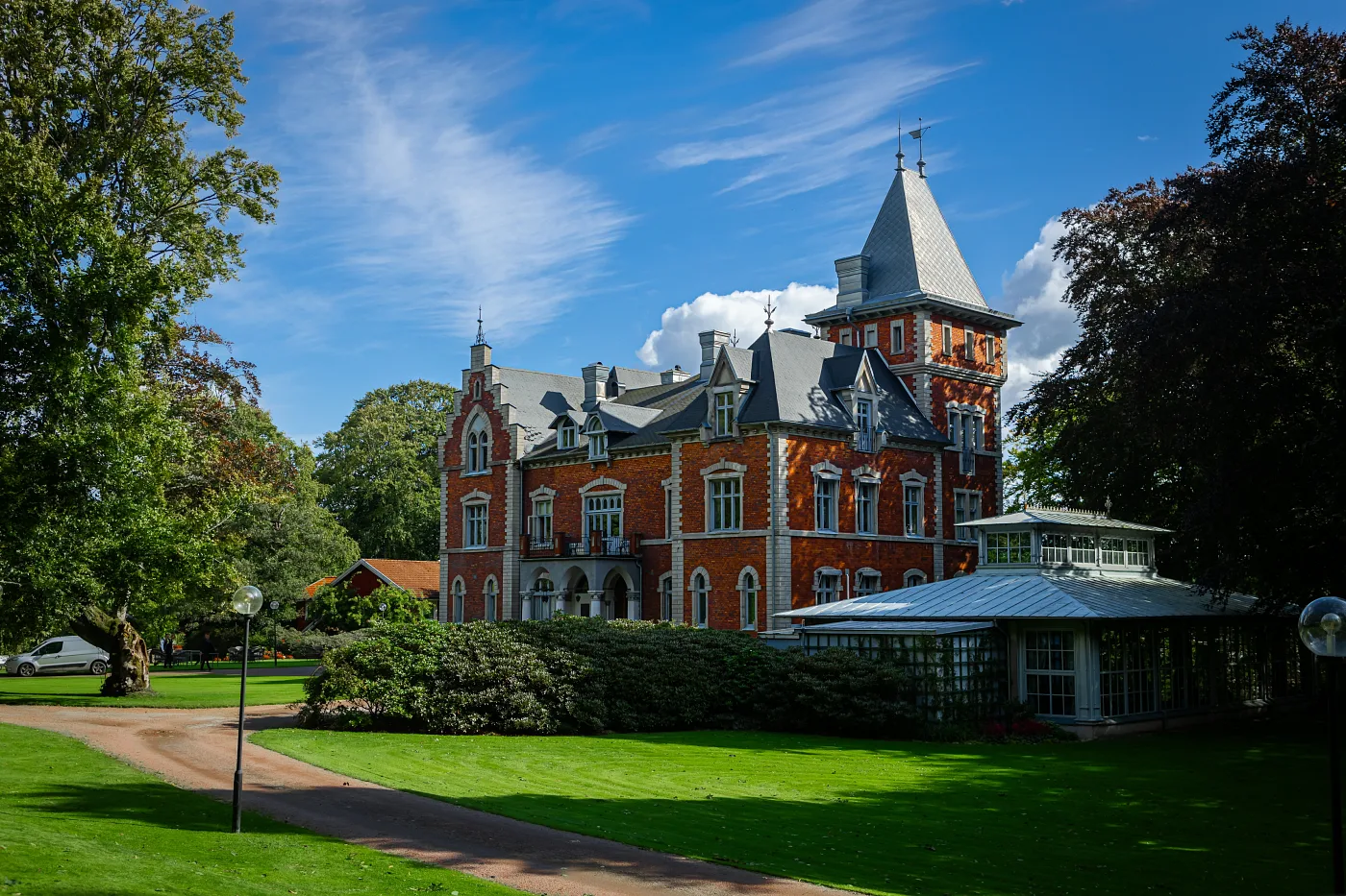 Herrgård i rött tegel med torn och glasveranda, gräsmatta och grusväg