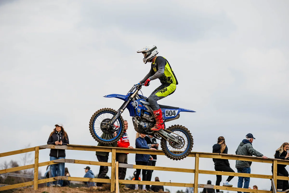 Motocross rider jumping past a wooden fence with spectators, Alingsås