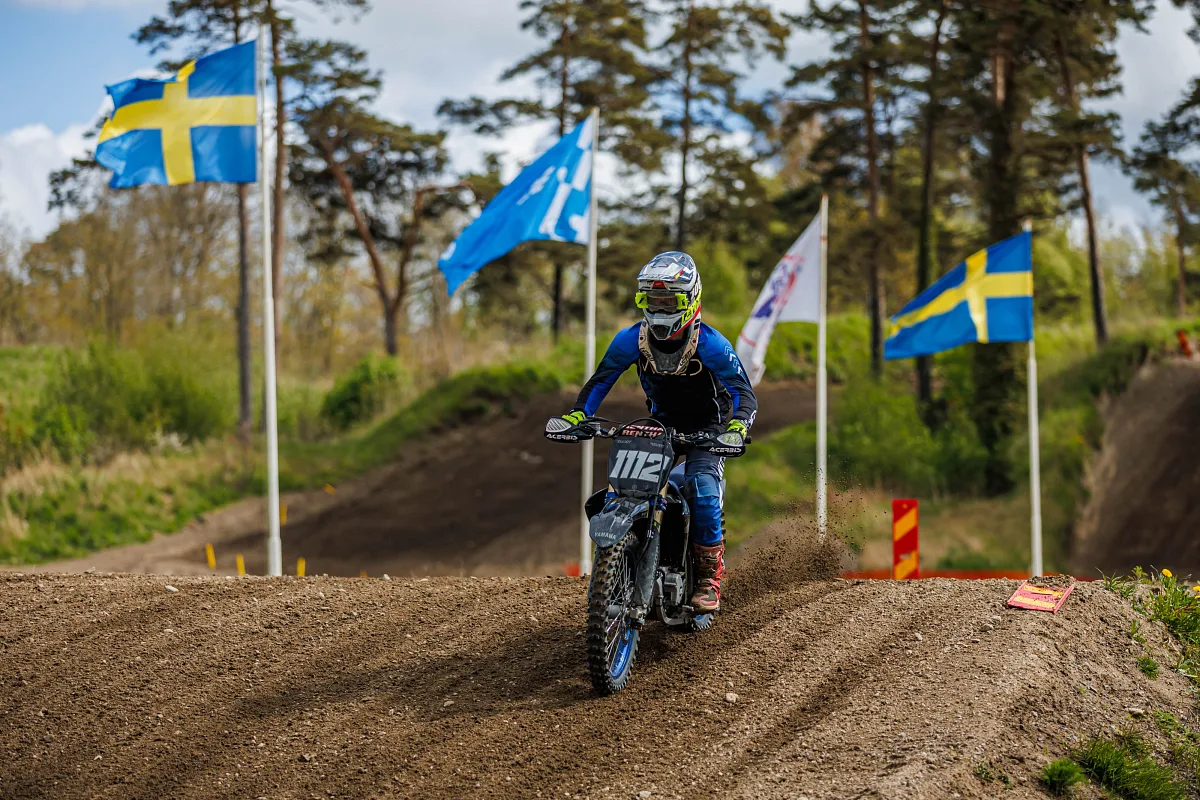 Motocross rider coming over a crest between Swedish flags, Varberg
