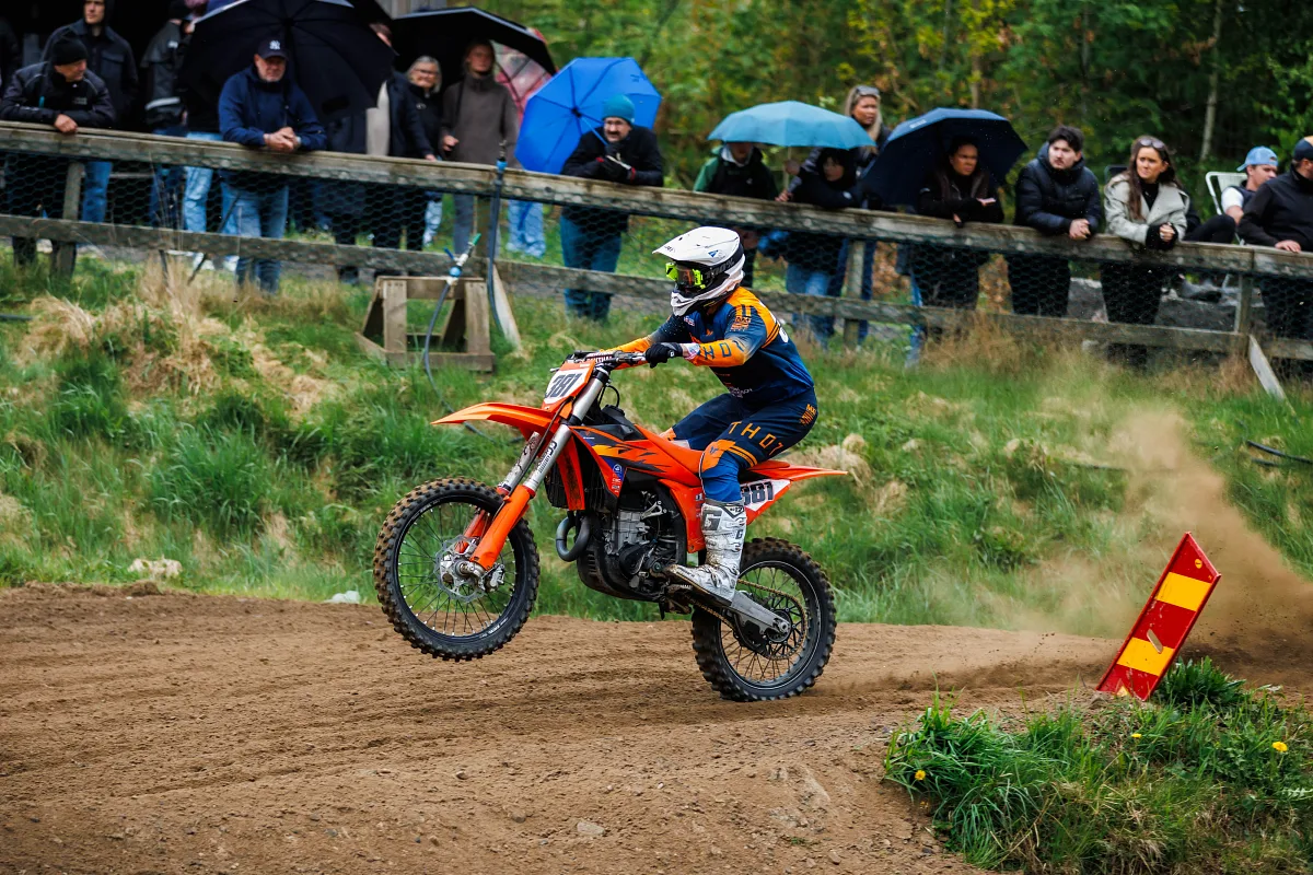 Motocross rider on an orange KTM with spectators in the rain behind the fence, Varberg