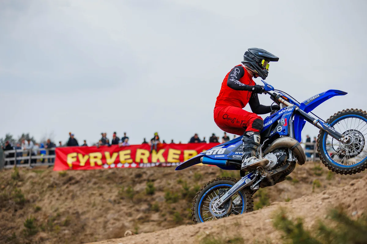 Motocross rider in red on a blue Yamaha climbing a hill in front of a Fyrverkeri banner and spectators, Alingsås
