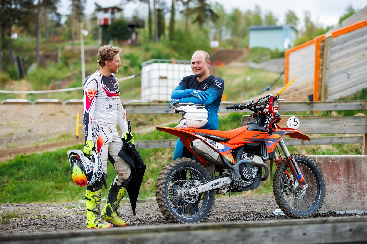 Motocross rider and team member talking next to an orange KTM in the paddock, Varberg