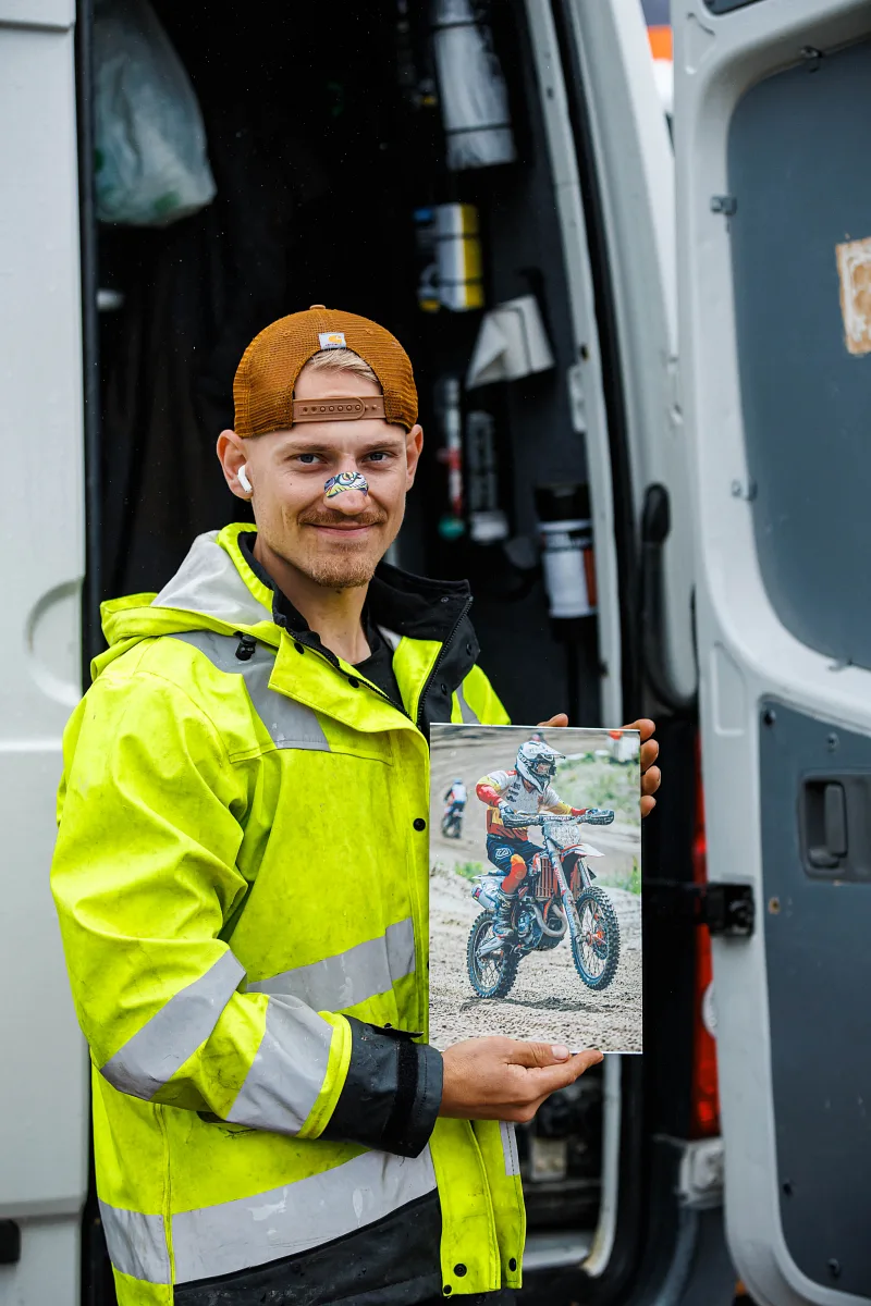 Man in a high-visibility jacket holding a printed photo of a motocross rider, Kinds