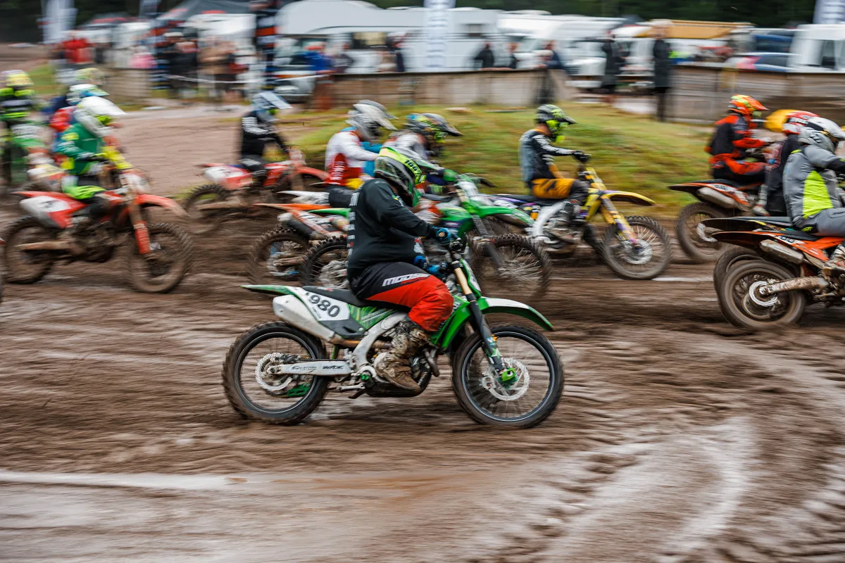 Motocross riders on a muddy track with the paddock in the background, Kinds